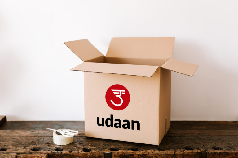 Udaan box on dark wooden table near tape and scissors