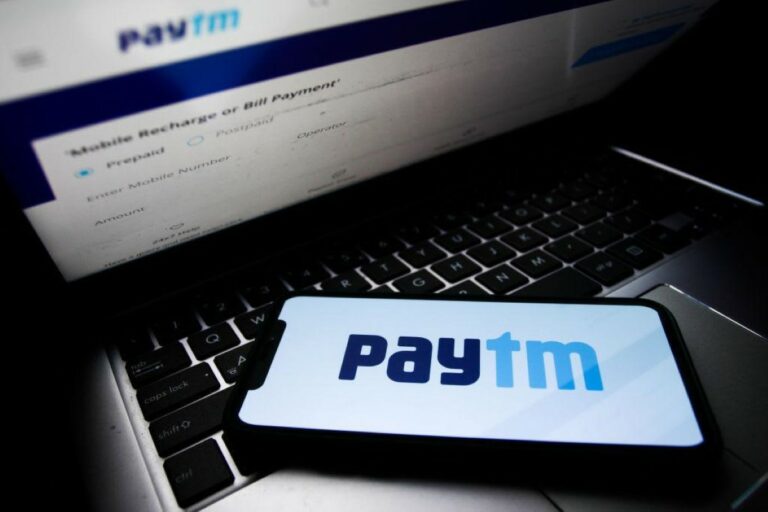Paytm logo displayed on a phone screen and Paytm website displayed on a laptop screen are seen in this illustration
