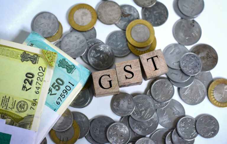 In this photo illustration Indian currency coins and fifty, twenty rupees notes are seen with a GST (Goods and Service Tax) cube blocks