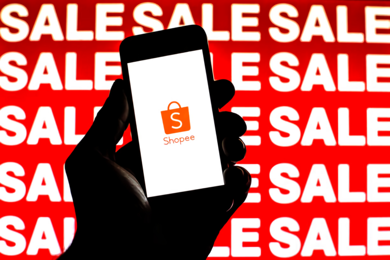 Shopee logo is seen on a smartphone screen with 'Sale' words in the background