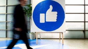 A passerby in front of board depicting Facebook like logo