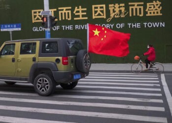 A vehicle flying a Chinese flag drives past a woman