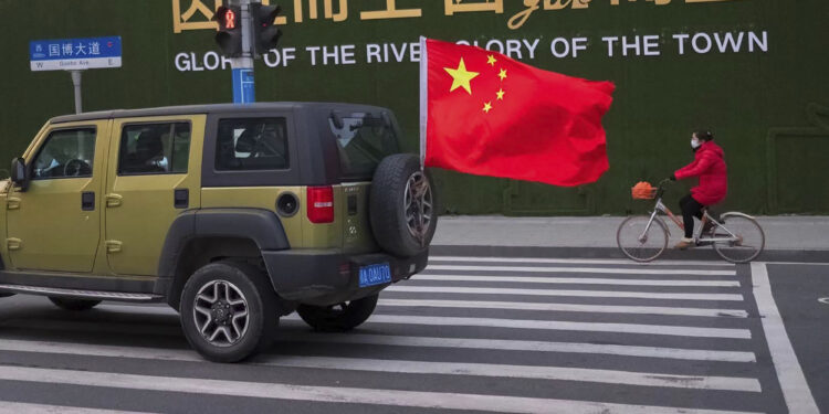 A vehicle flying a Chinese flag drives past a woman