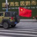 A vehicle flying a Chinese flag drives past a woman