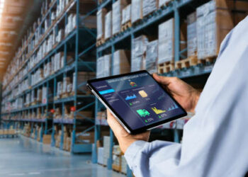 Manager using digital tablet,showing warehouse software management dashboard on blurred warehouse as background