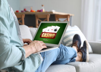 Young man with laptop playing in casino online at home